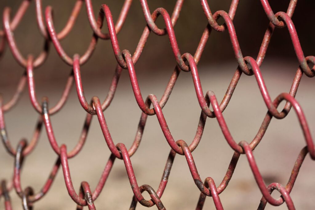Detailed view of a red rusty chain link fence, highlighting texture and pattern.