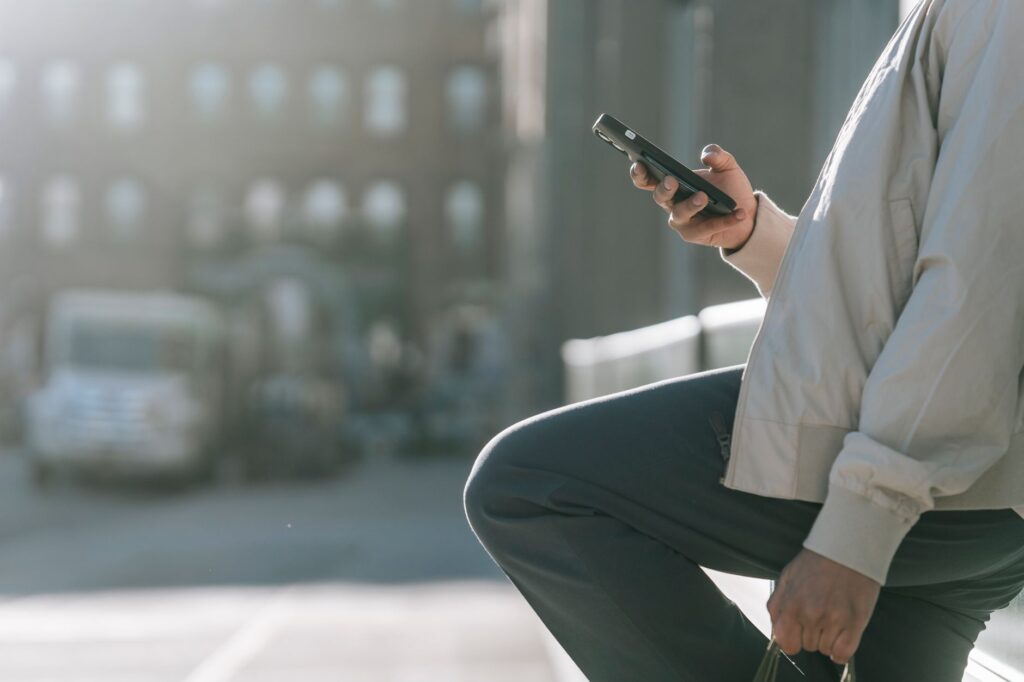 Side view of crop unrecognizable male with raised leg surfing internet on cellphone on roadway in sunny city