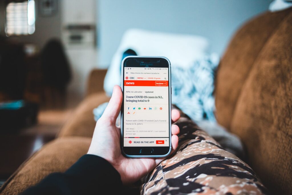 A person browsing news on a smartphone while relaxing on a sofa indoors.